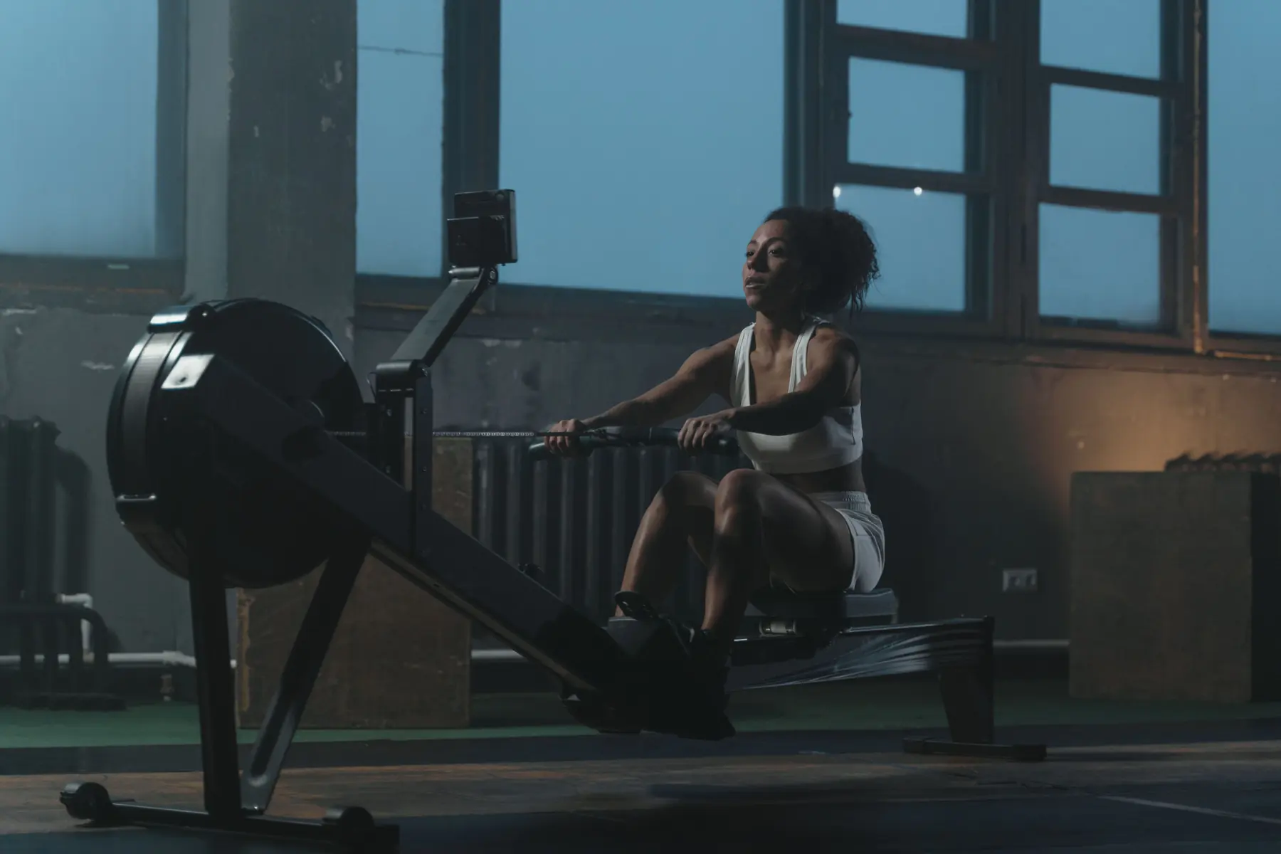 An athlete rows on an indoor rower beside the warehouse windows