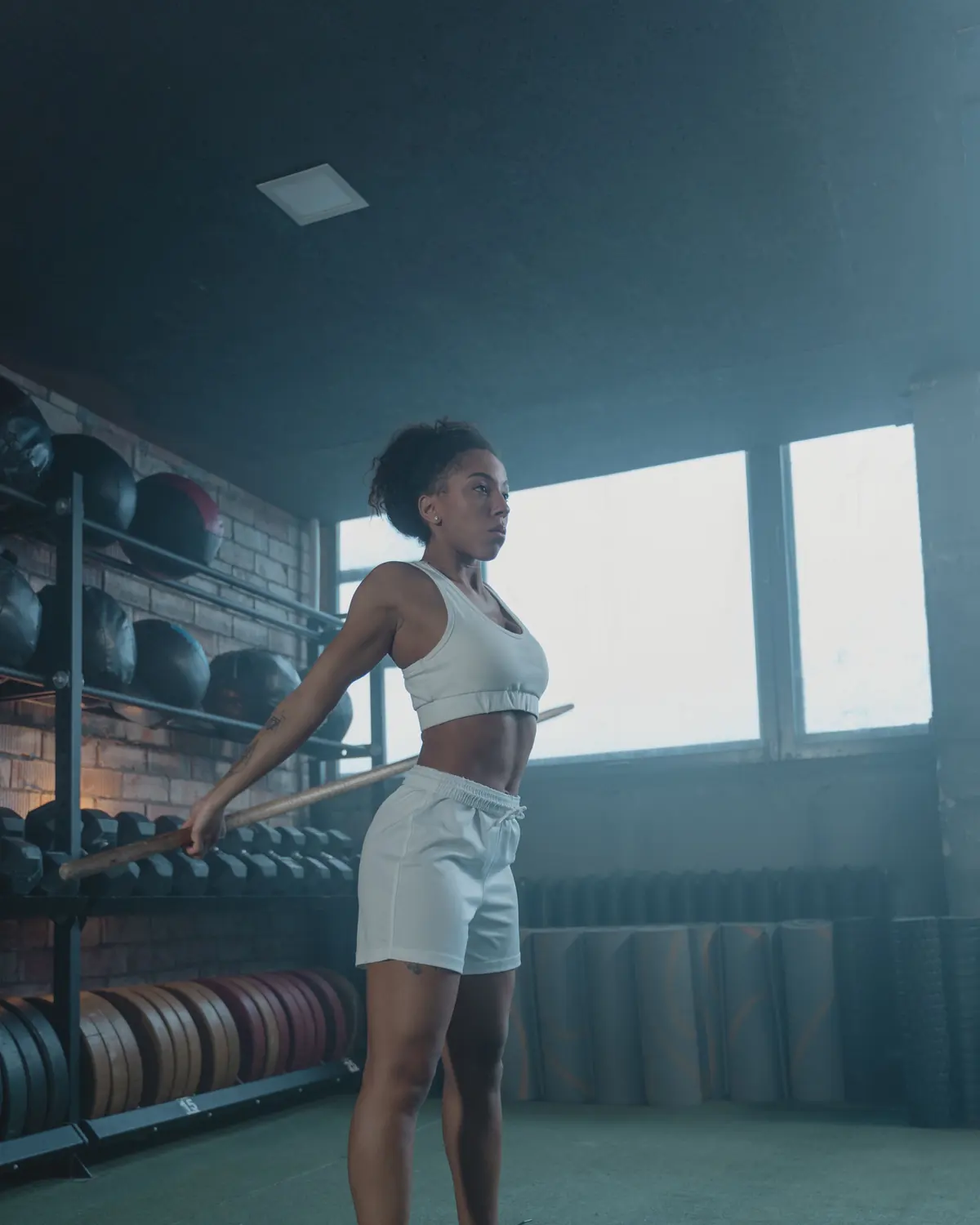 An athlete rehearses a lift with a wooden dowel in front of the dumbbell rack